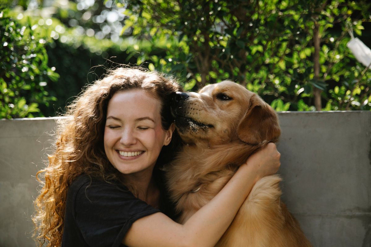 Happy golden retriever being hugged by a smiling woman in a sunny park