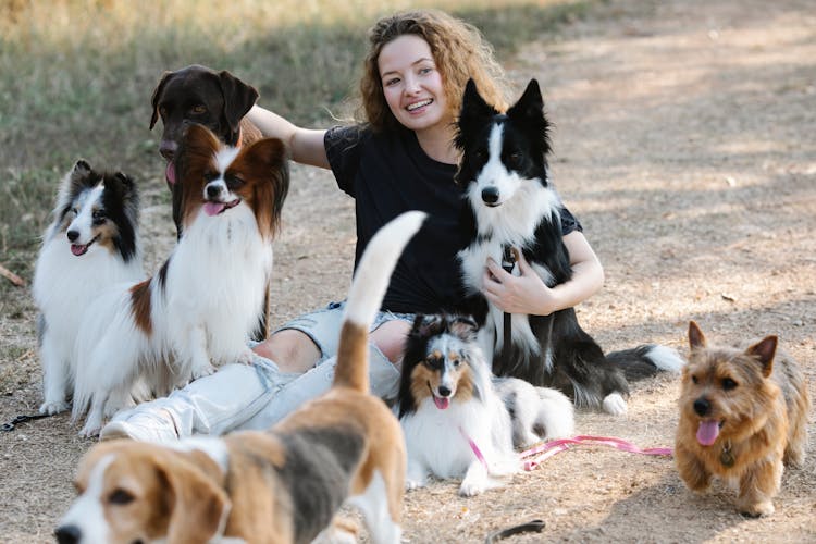 Glad Young Woman With Dogs Sitting On Countryside Road