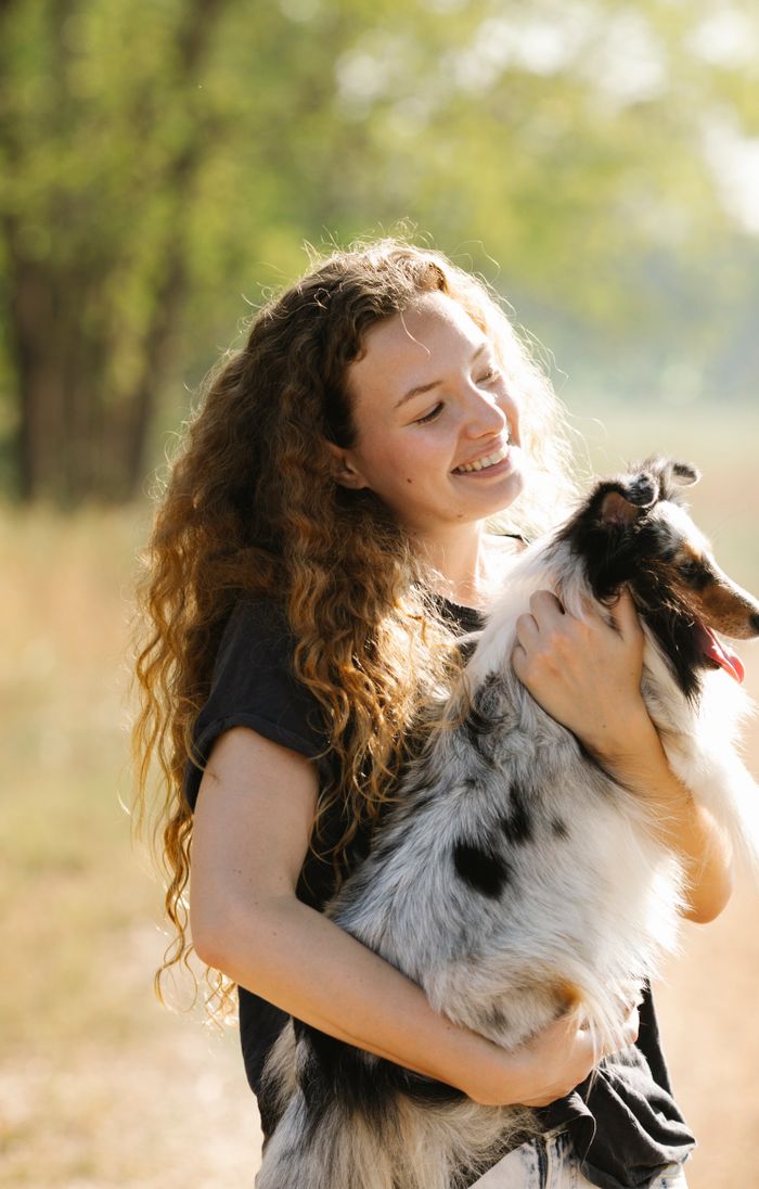 Smiling young woman holding her happy dog outdoors