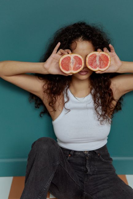 Woman playfully holding grapefruit halves over her eyes in a fun portrait.