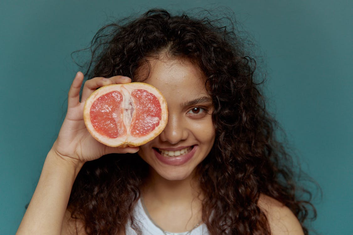 Free Close-Up Photo of a Woman with Curly Hair Holding a Sliced Grapefruit Stock Photo