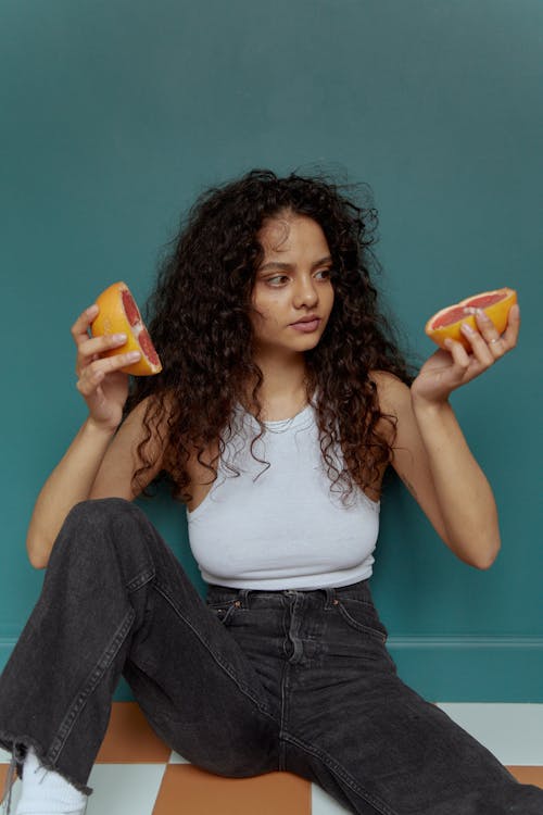 Free A Woman in White Tank Top Sitting on the Floor while Holding a Sliced Fruit Stock Photo
