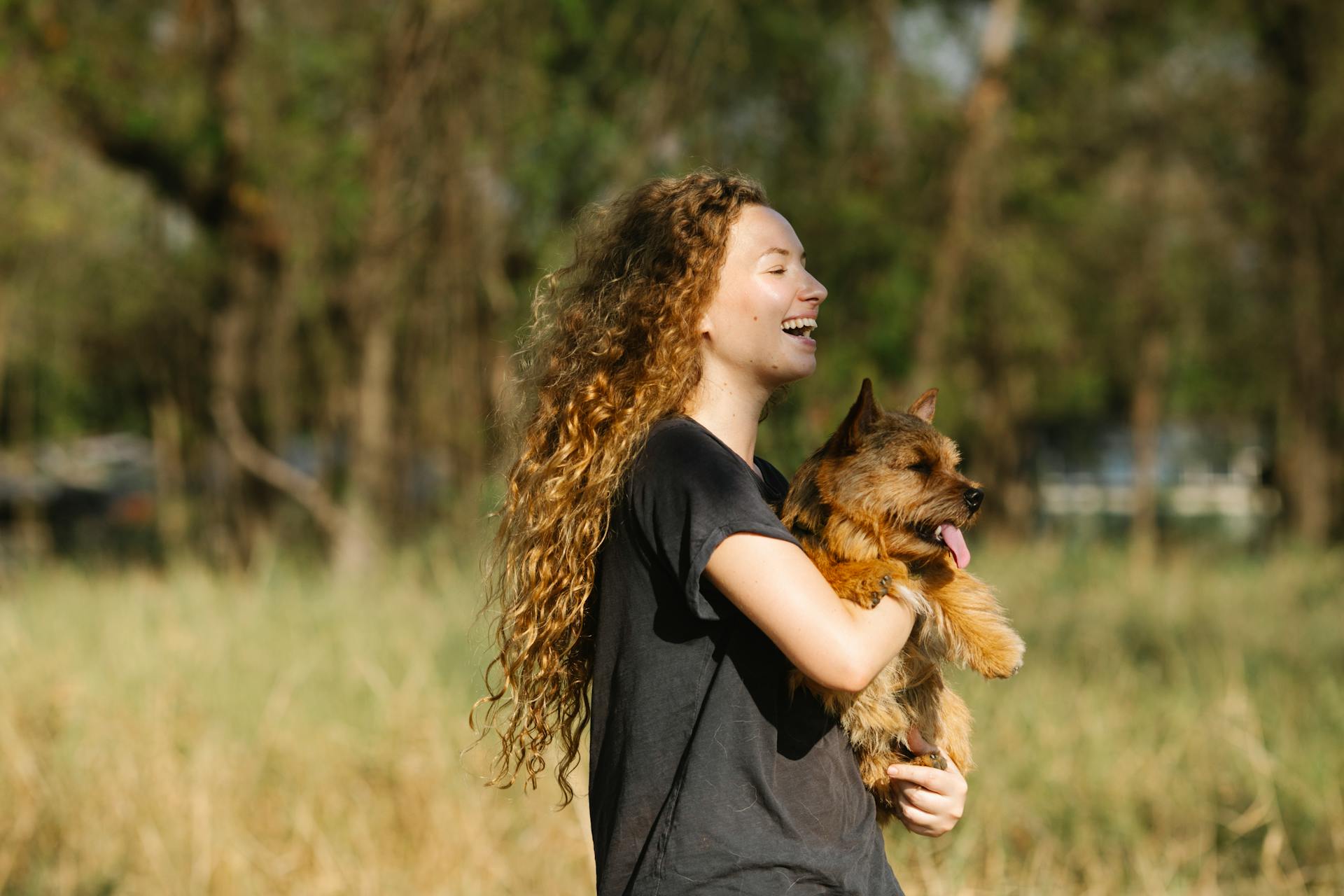 En leende kvinna bär på en liten hund i en park