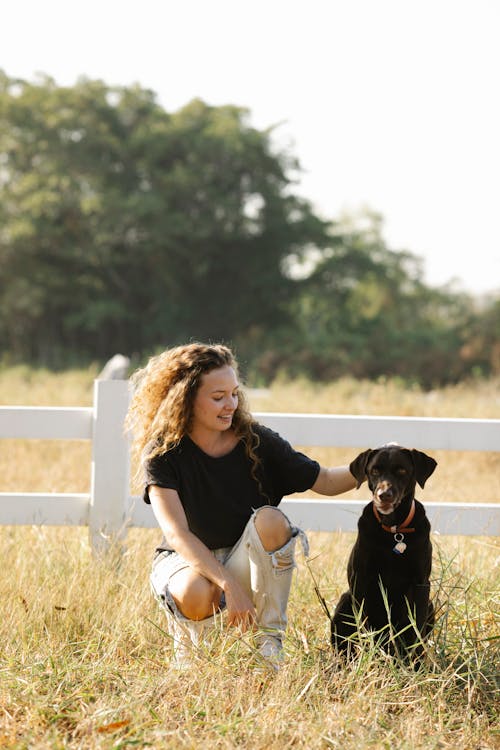 Smiling owner caressing Labrador Retriever on lawn in countryside