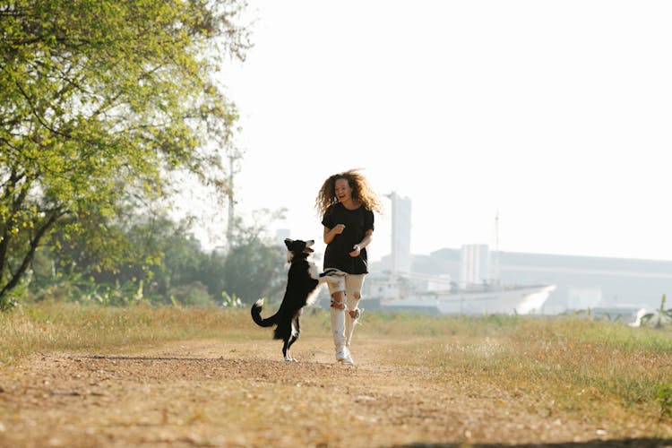 Happy Woman Playing With Border Collie On Path In Town