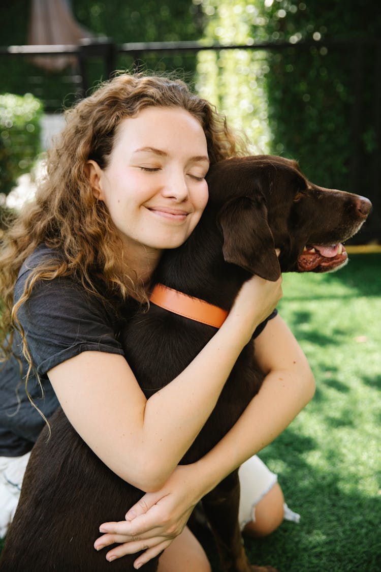 Dreamy Woman Embracing Labrador Retriever On Lawn