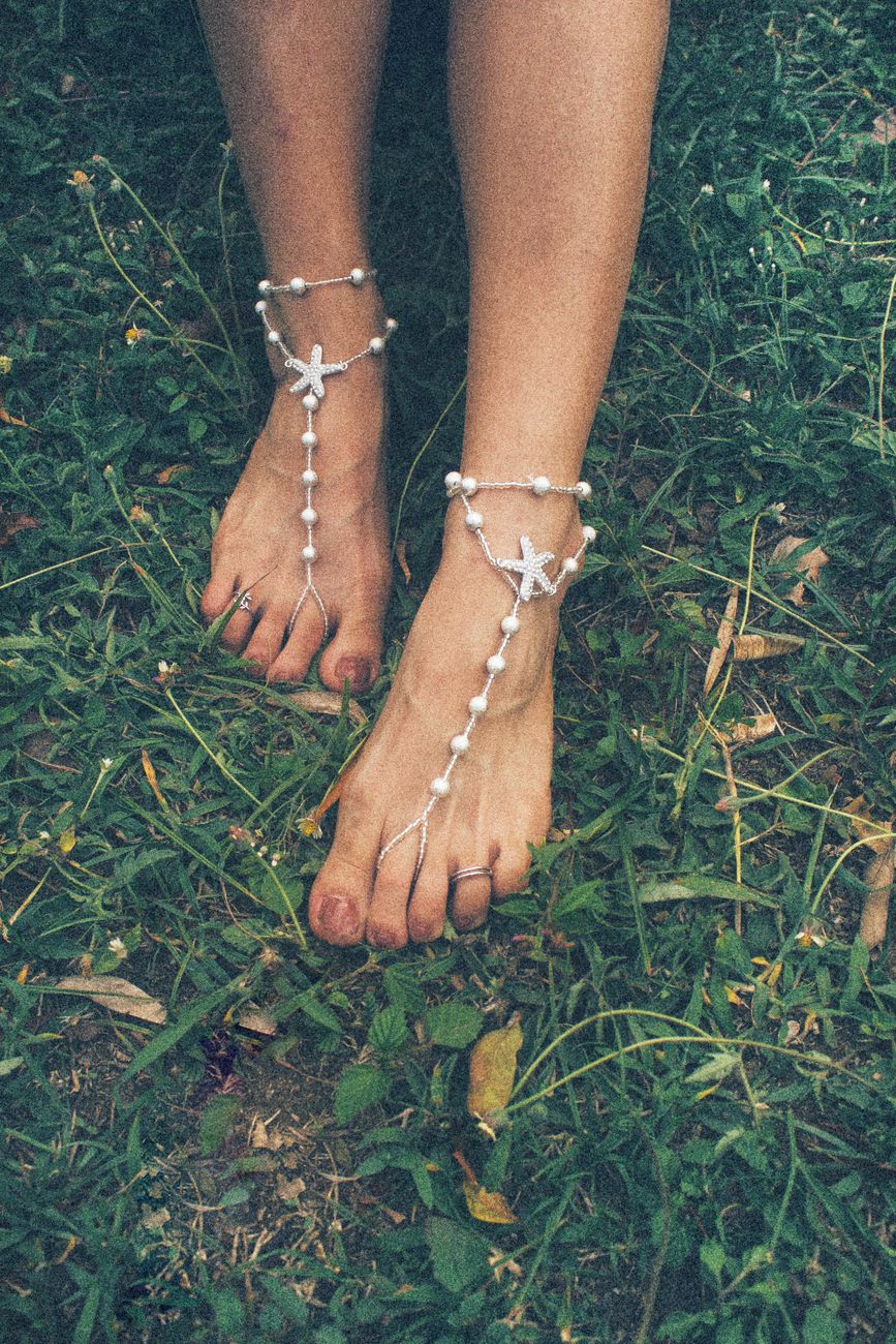 Close-up of bare feet adorned with boho-style jewelry on grass, creating a natural and artistic vibe.