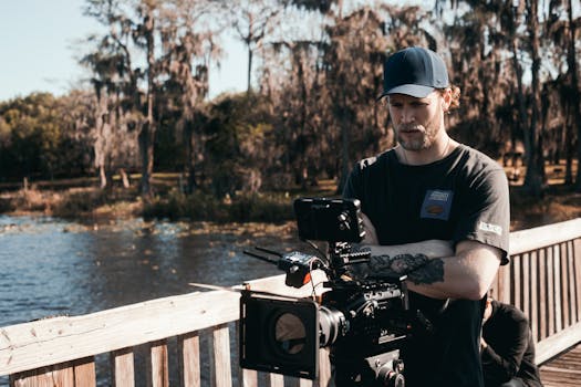 Cinematographer operating camera gear on outdoor film set by a scenic lake.