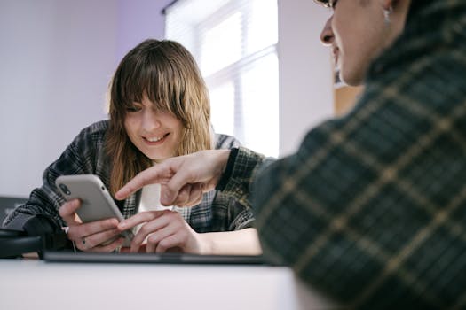 Two friends sharing a moment while using a smartphone indoors. Casual and joyful interaction.