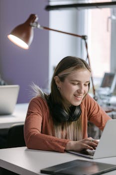 A cheerful young woman working on her laptop in a modern office setting.