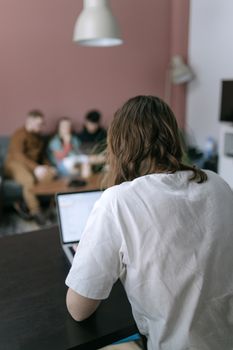A person using a laptop in an open-plan home environment with others in the background, casual setting.