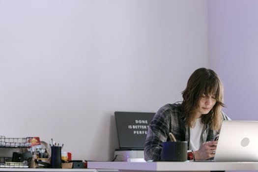 Young professional using a smartphone at a desk in a modern office setting.