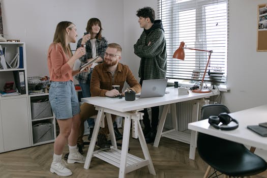 A group of young professionals discussing ideas in a modern office with laptops and coffee.