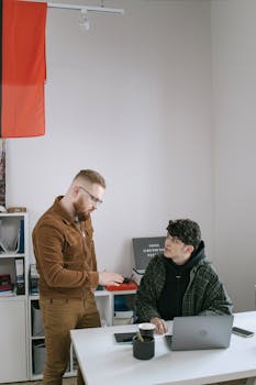 Casual office scene with two coworkers discussing a project in a modern workspace.