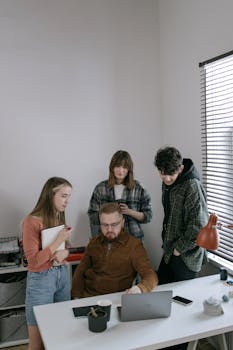 Group of young professionals collaborating around a desk with laptops in a modern office setting.