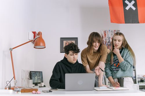 Free A group of young adults working together in a modern office, focused on a laptop screen, illustrating teamwork and innovation. Stock Photo