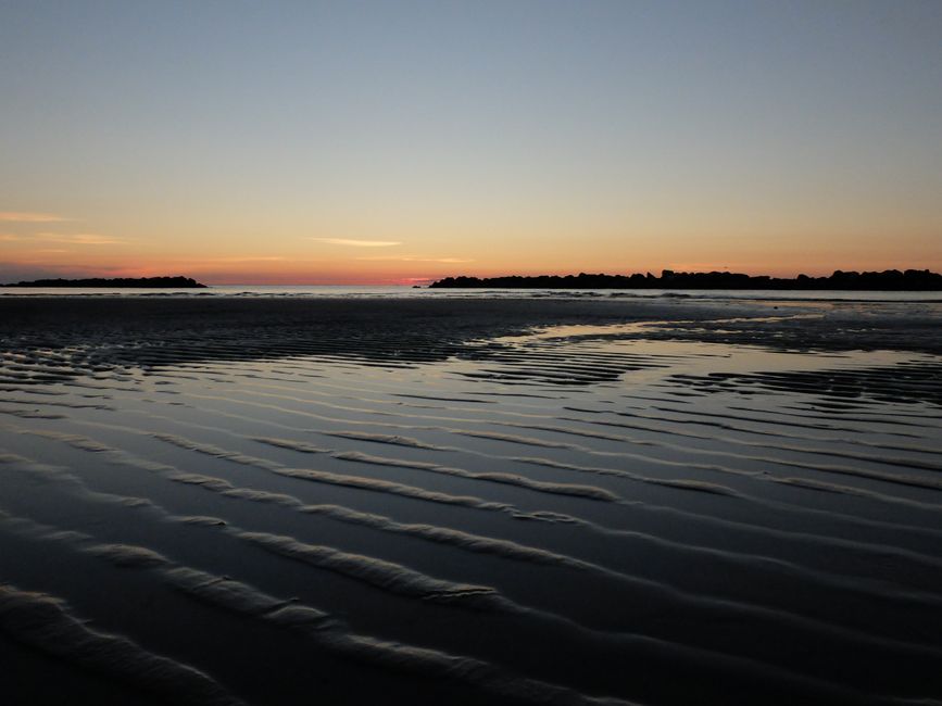 Peaceful sunset on a quiet beach with rippling sand and calm waves.