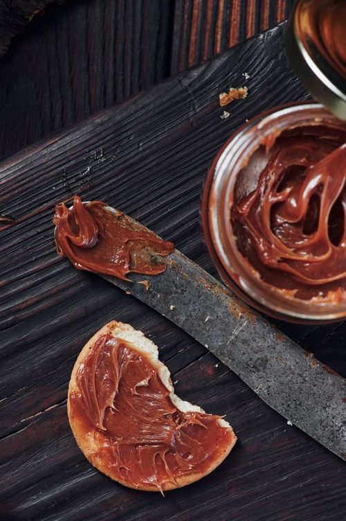 Free Close-up of chocolate spread on bread with a knife on a rustic wooden surface. Stock Photo