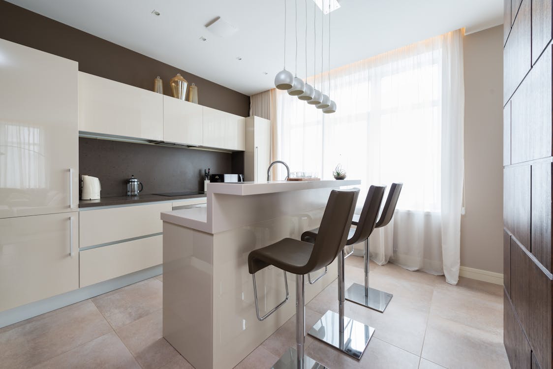 Free Kitchen bar counter in island with bar chairs in center of light kitchen with modern appliances and white glossy cabinets Stock Photo