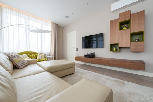 Interior of spacious living room with comfortable sofa with pillows and TV hanging on wall in luxury apartment