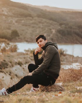 Young man sitting outdoors in nature near a serene lake during the daytime.