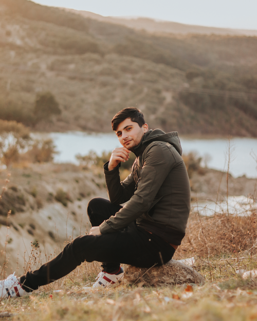 Free Young man sitting outdoors in nature near a serene lake during the daytime. Stock Photo