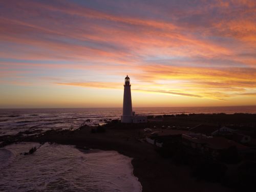 Free Peaceful sunset view of La Paloma lighthouse with vibrant sky reflecting over the ocean. Stock Photo