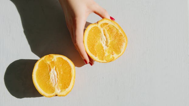 A hand holds vibrant orange slices in a sunlit flatlay, creating summer vibes.