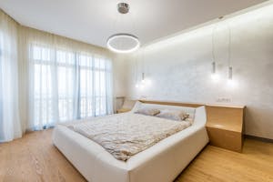 Interior design of minimalistic modern bedroom furnished with comfortable bed and bedside nightstands decorated with ring shaped chandelier and lamps on ceiling