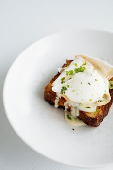 A delicious gourmet toast topped with poached egg and creamy sauce on a white plate.
