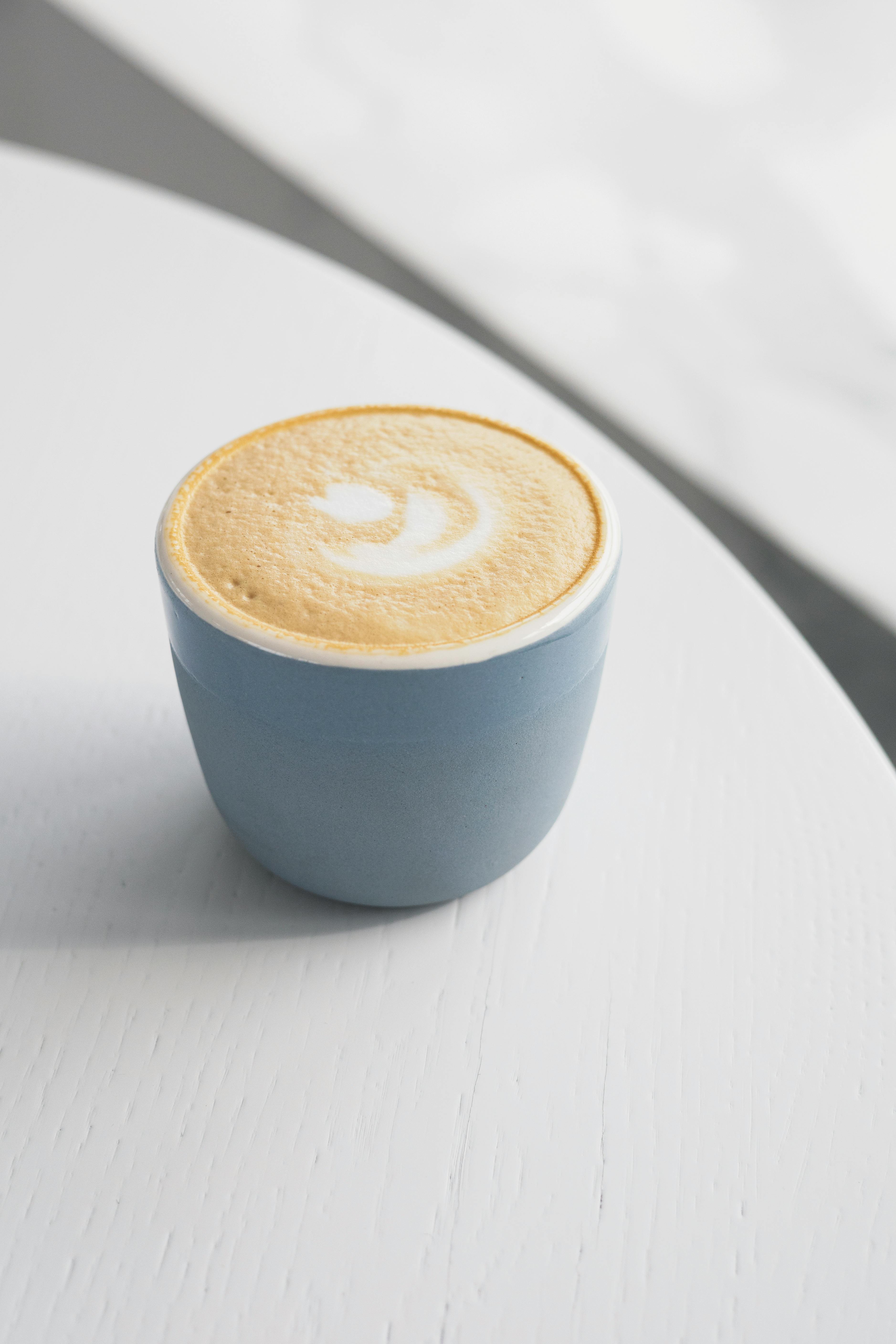 Elegant flat lay of a latte in a blue cup, showcasing intricate latte art on a smooth white surface.