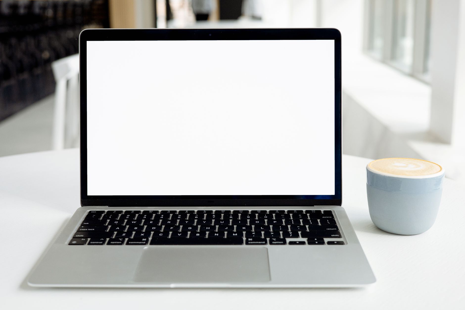 A minimalist indoor workspace featuring a blank laptop screen and a cappuccino in a modern setting.