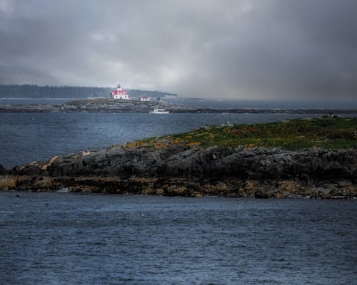 Breathtaking scenery of aged Egg Rock Light lighthouse located on cape in wavy ocean against overcast sky on rainy day