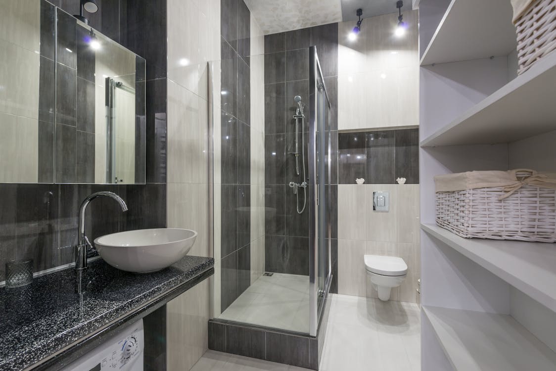 Interior de baño moderno y luminoso. Parte de la habitación con un lavabo  blanco con grifo de agua, estante, ducha y un espejo redondo en la pared  blanco-negro Fotografía de stock 