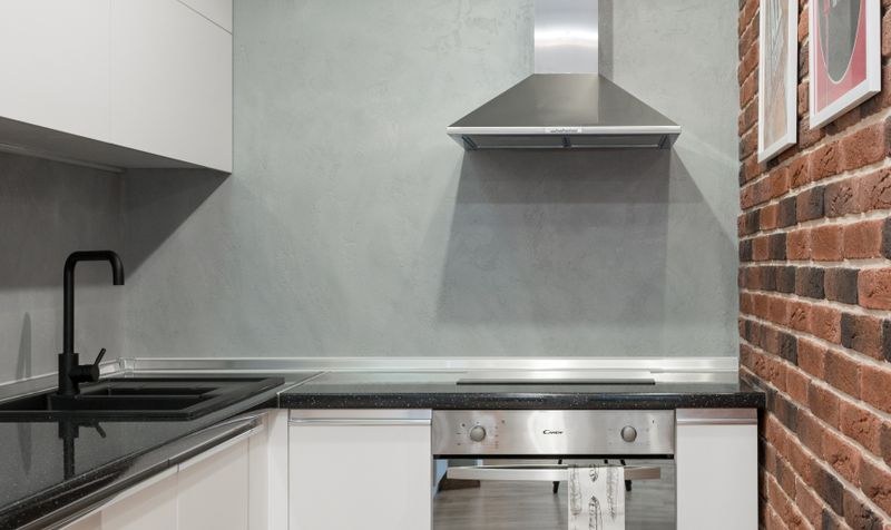 Stainless steel wall-mount range hood in a modern kitchen with brick wall