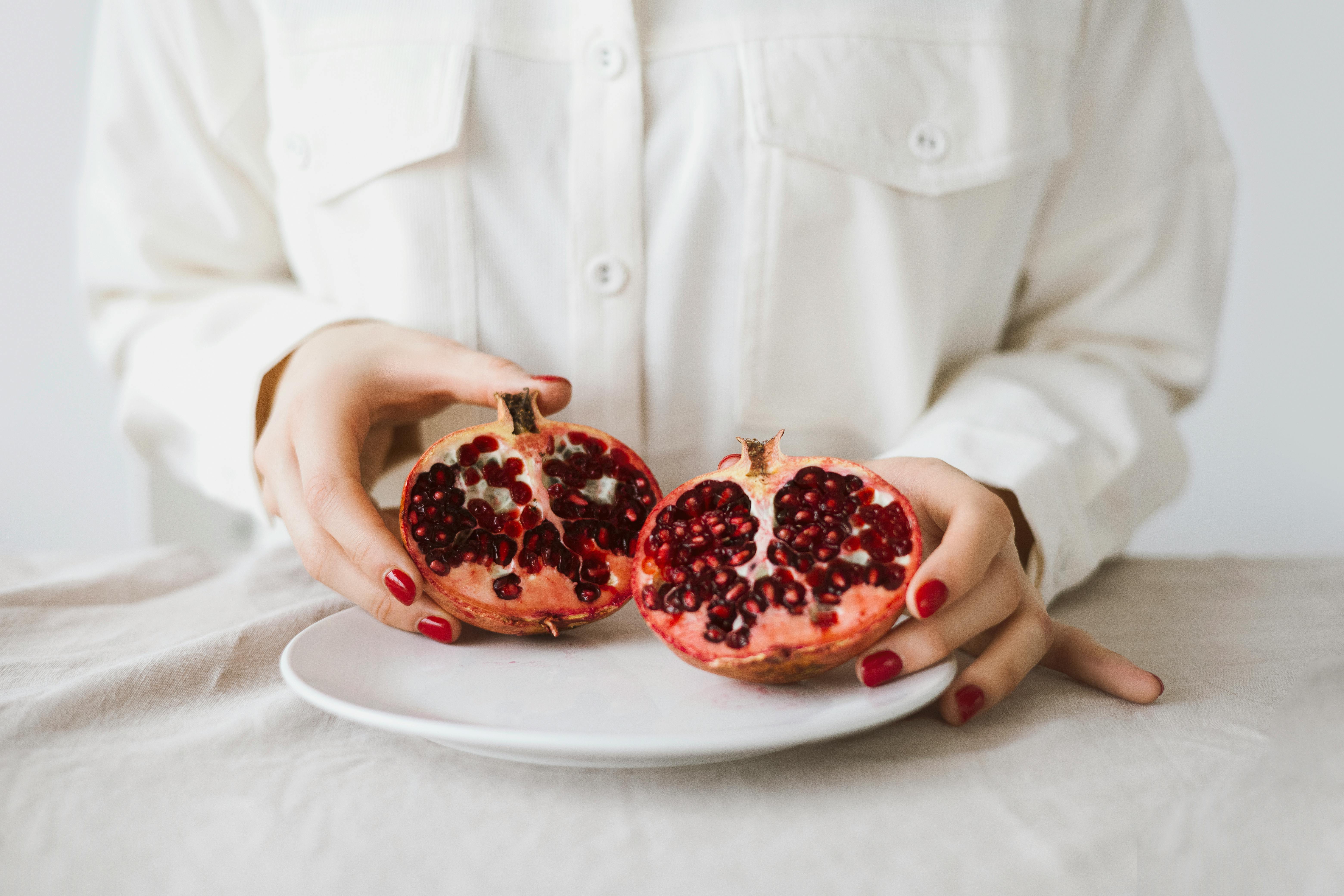 Hands holding a freshly sliced pomegranate on a plate, showcasing its vibrant seeds.