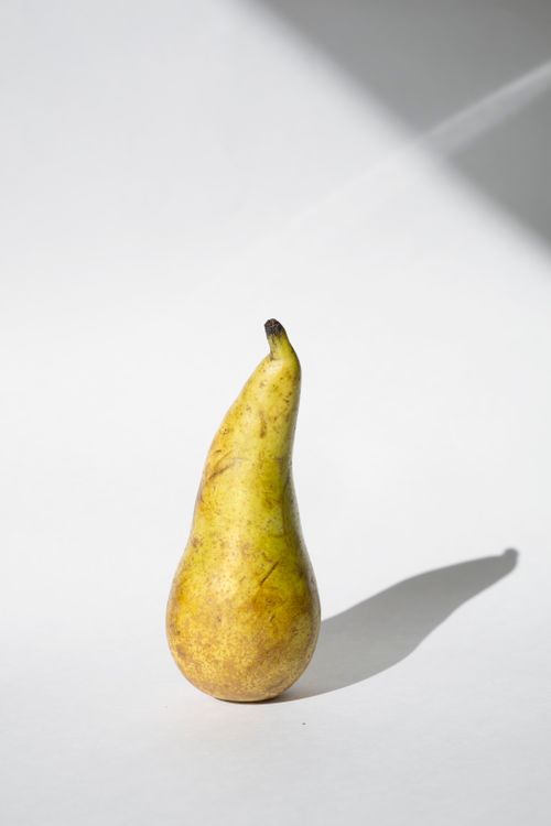 Free A solitary pear casting a shadow on a white background, minimalist aesthetic. Stock Photo