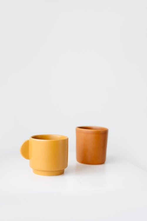 Bright yellow and orange ceramic cups placed on table against white background in daylight