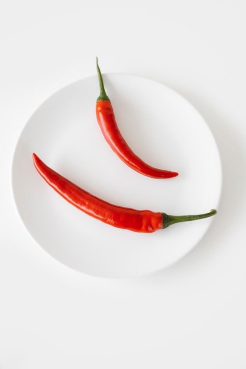 Free Two vibrant red chili peppers arranged on a white plate for a minimalist, fresh look. Stock Photo