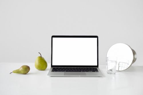 Free A minimalist desk setup featuring a laptop, pears, and a mirror for a modern look. Stock Photo