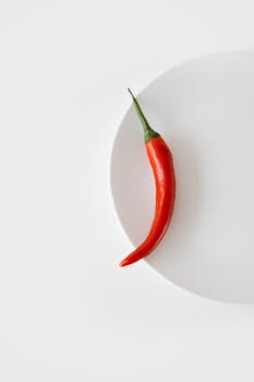 Minimalist photo of a single red chili pepper on a white plate, emphasizing spice and simplicity.