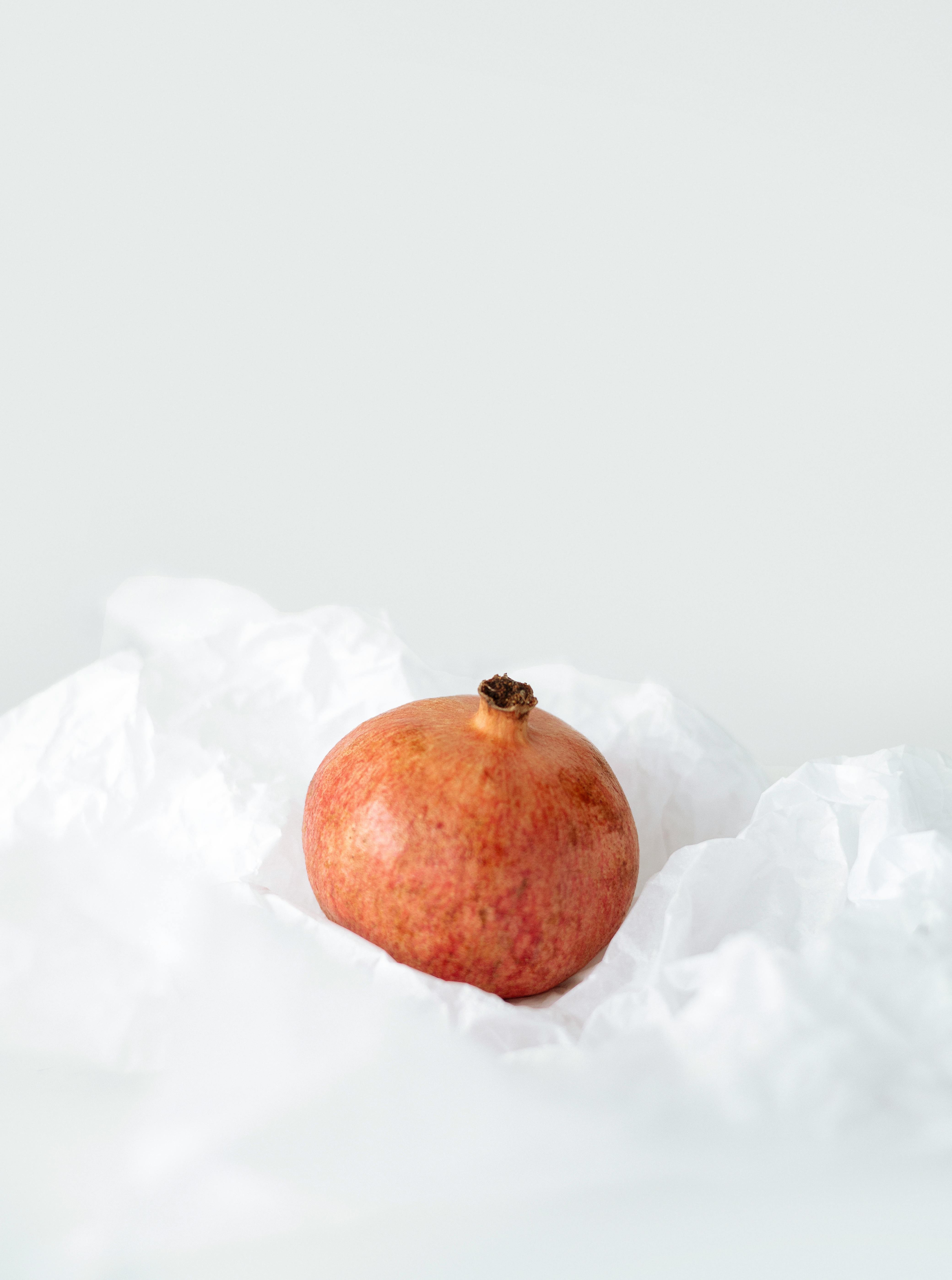 A single pomegranate elegantly placed on white textured fabric, showcasing simplicity.