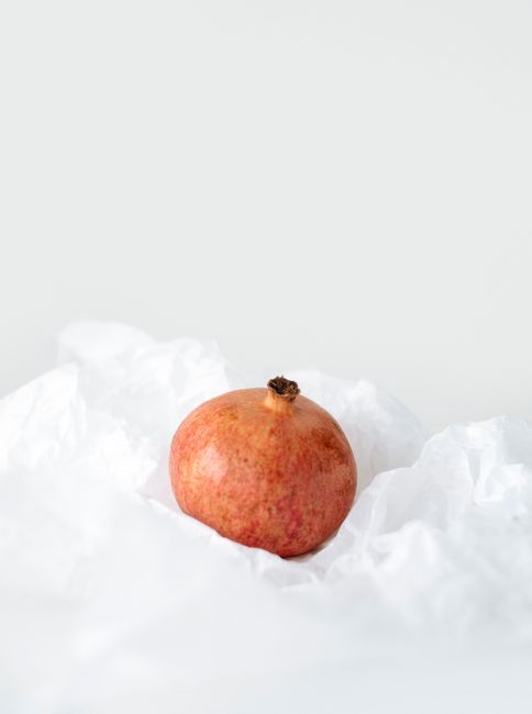 A single pomegranate elegantly placed on white textured fabric, showcasing simplicity.