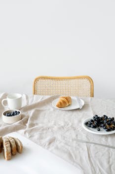 Minimalist breakfast setup with croissant and blueberries on a neutral tablecloth, evoking a serene morning.