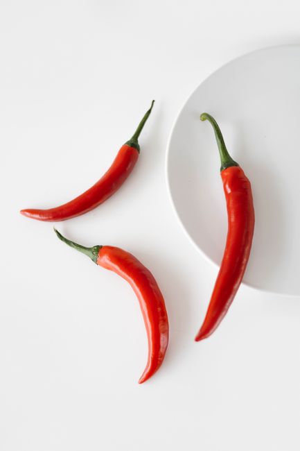 Close-up of vibrant red chili peppers on a minimalist white background, showcasing spicy flavor.