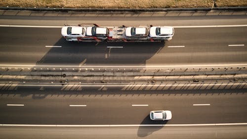 Aerial view of truck transporting cars moving on asphalt road with marking lines and auto