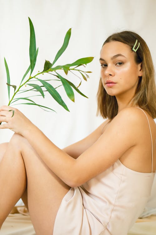 Side view of gentle female in dress with hair pin and estragon plant sprig looking at camera