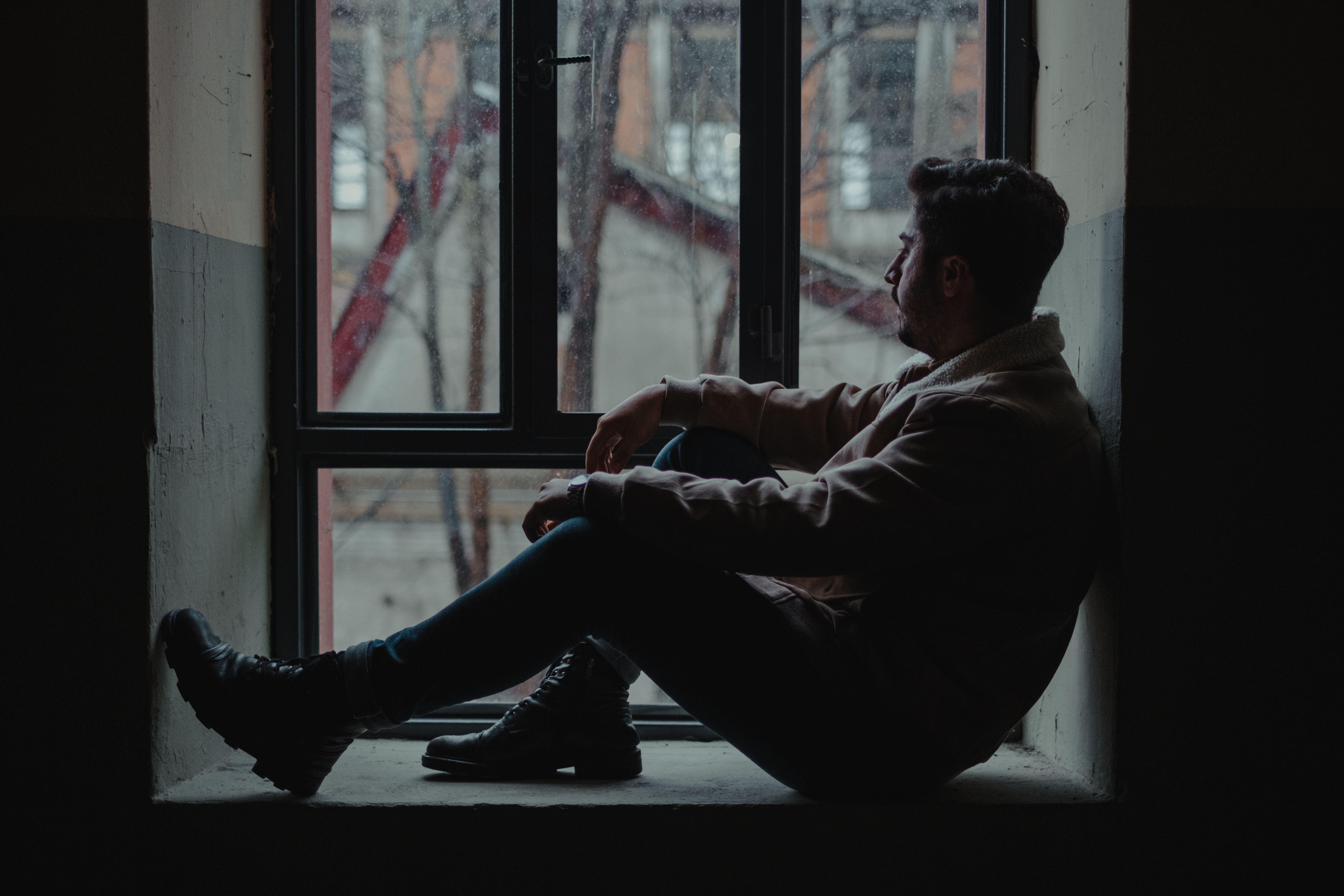 Man in his 40s sitting thoughtfully near a window, reflecting on low energy and mood