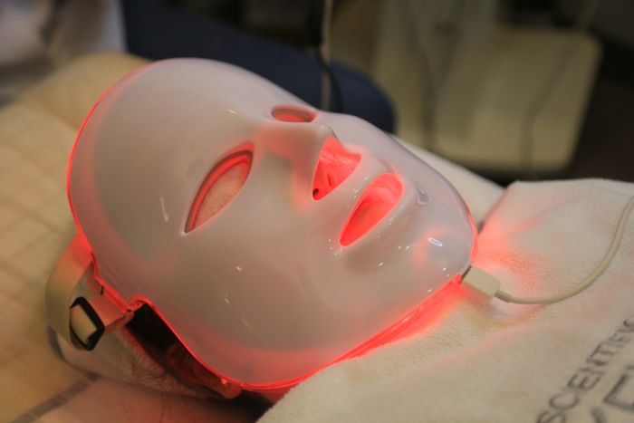 Client resting beneath a red LED light therapy mask