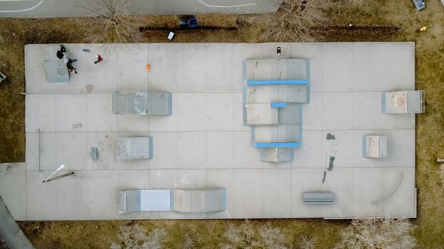 Aerial view of anonymous skaters interacting on skate ramp between leafless trees on lawn in daylight